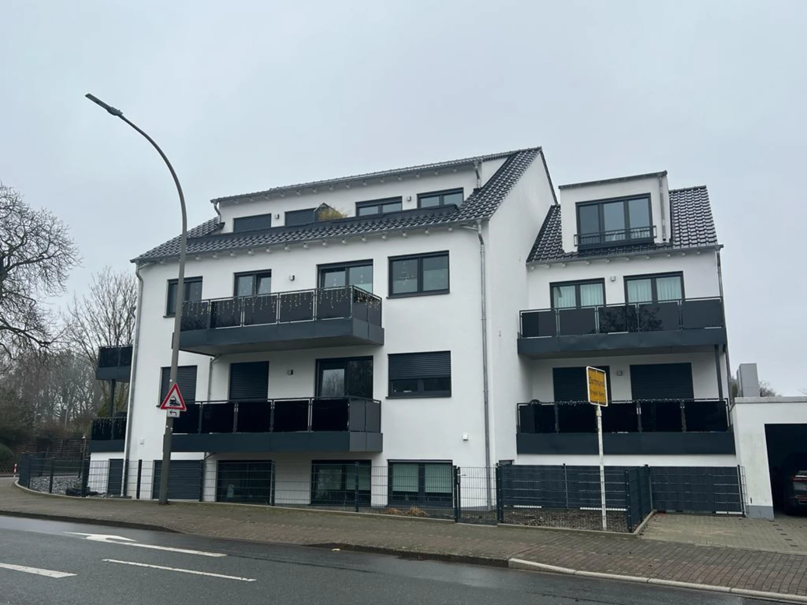 Elewacja budynku po remoncie domu z czarnymi balkonami i panelowym ogrodzeniem