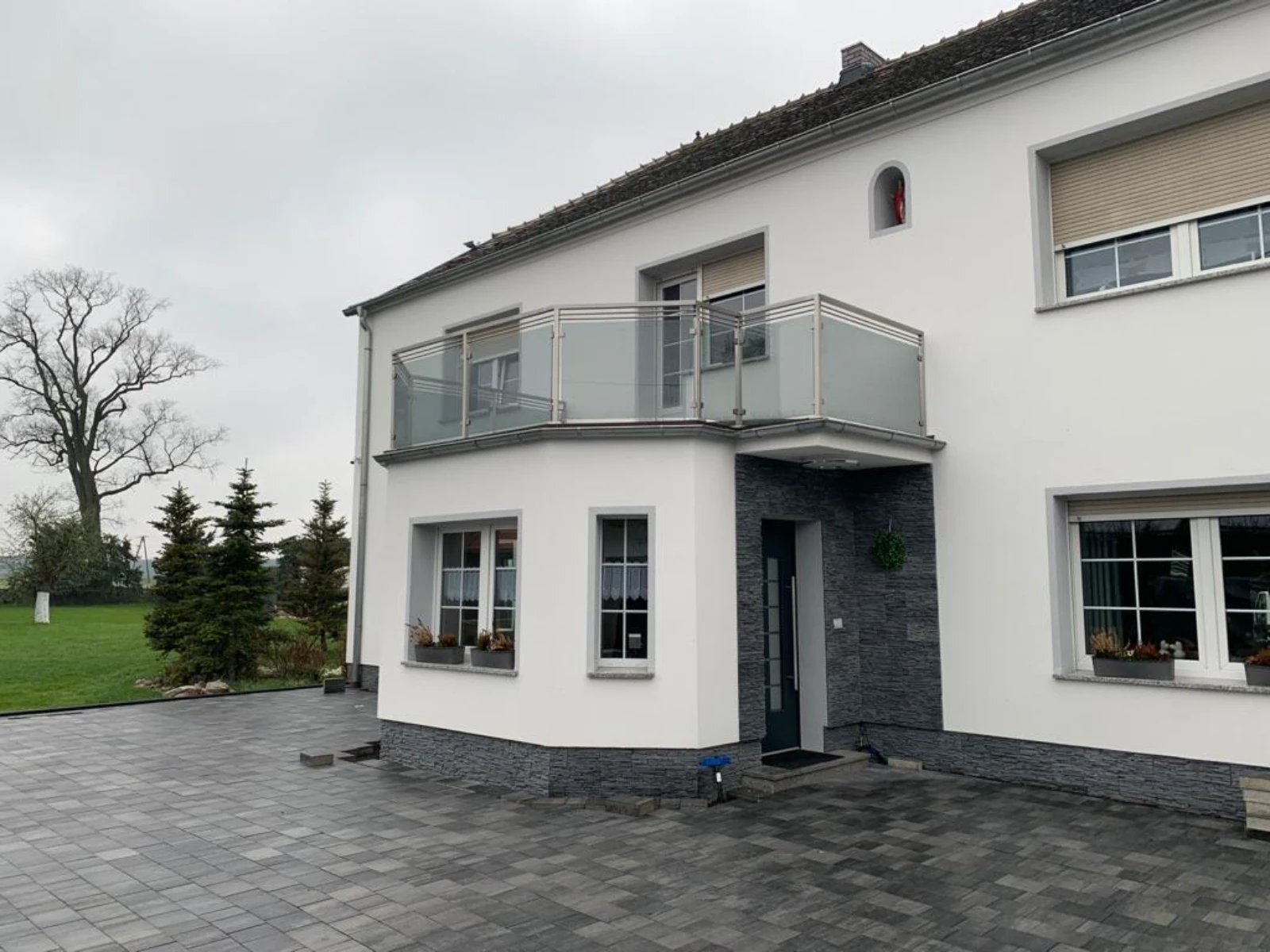 Odnowiona elewacja i nowy podjazd z szarej kostki brukowej przed domem z balkonem, Remont domu