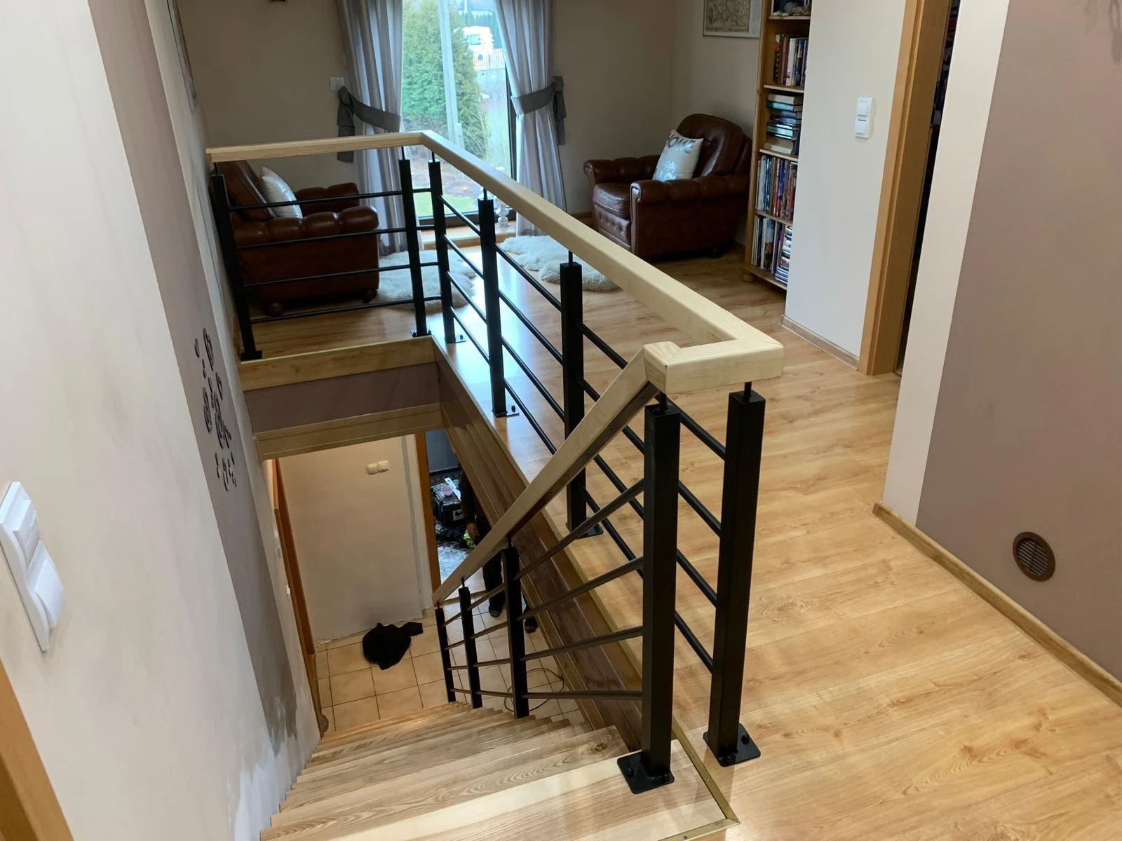 Układanie paneli: drewniane schody i korytarz z jasnymi panelami podłogowymi i czarną metalową balustradą