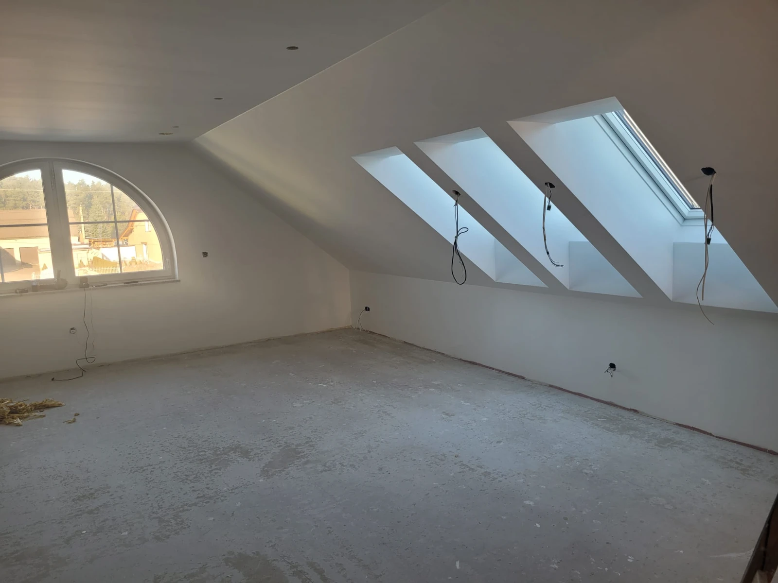 Pusta adaptacja poddasza z białymi ścianami, trzema oknami dachowymi i łukowym oknem