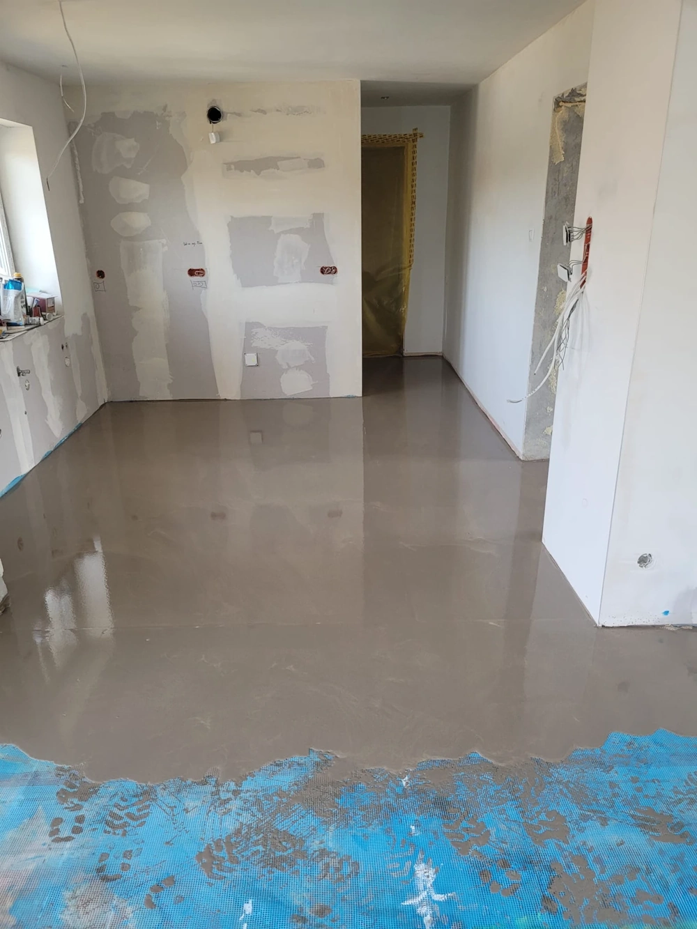 Wylewki w otwartym pomieszczeniu mieszkalnym – gładka, świeżo wykonana posadzka samopoziomująca i przygotowane ściany