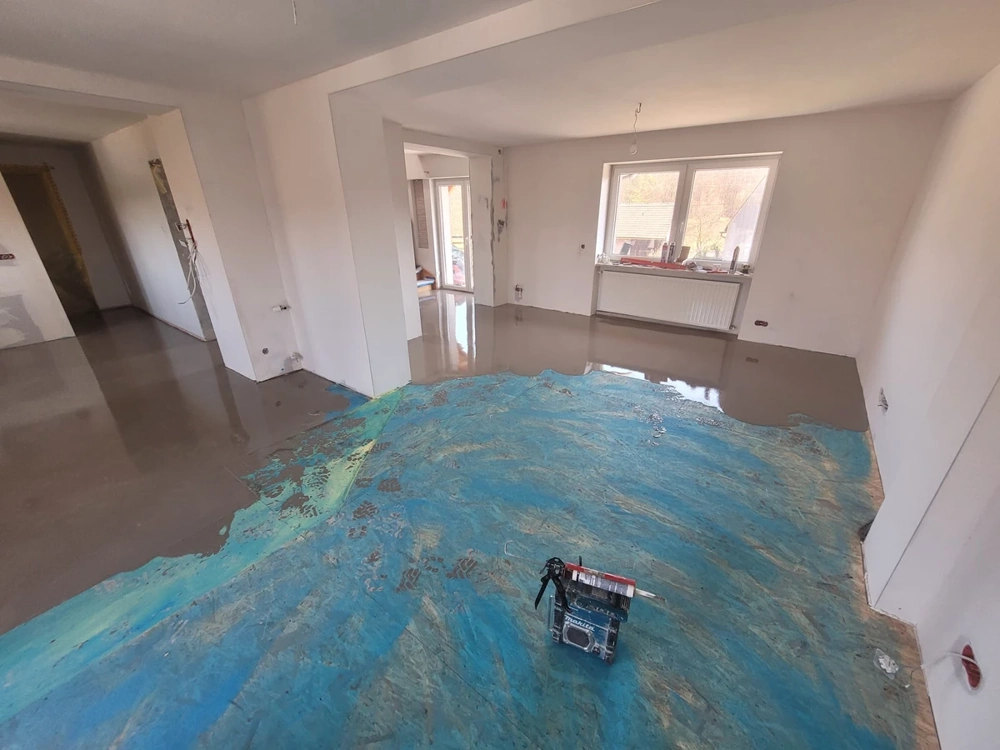 Wylewki samopoziomujące w salonie – wilgotna posadzka na niebieskiej folii i sprzęt do wylewania